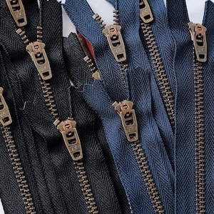 May include: Close-up of a group of black and navy blue zippers with antique brass pulls. The zippers are arranged in a vertical stack.
