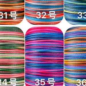 May include: Close-up of six spools of colorful thread. Each spool is labeled with a number in white text. The threads are in various colors, including orange, blue, green, pink, and purple. The threads are tightly wound.