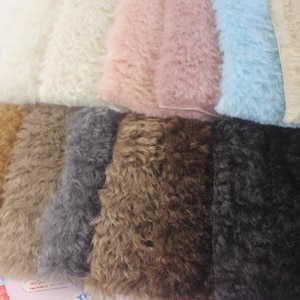 Puede incluir: Muestras de tela de piel sintética en varios colores. Las muestras incluyen crema, rosa, azul claro, beige, dorado, gris, marrón y negro. La piel tiene un pelo largo y texturizado, y la tela está dispuesta en filas.