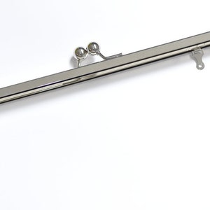 May include: A silver metal purse frame with two round knobs on the top. The frame is designed to be used for a purse or clutch.