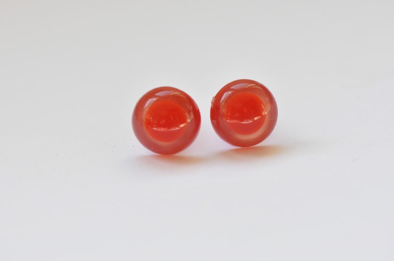 Puede incluir: Un par de peque&ntilde;os pendientes redondos de vidrio rojo y naranja. Los pendientes son transl&uacute;cidos y tienen un acabado ligeramente iridiscente.