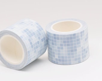 May include: Two rolls of decorative washi tape. The tape features a repeating pattern of small, light blue squares, creating a mosaic-like design. The rolls are cylindrical with a white interior, perfect for crafts and adding a decorative touch.