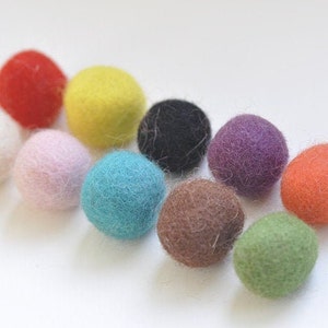 May include: Ten felt balls in various colours, including red, yellow, white, pink, blue, brown, purple, orange, and green. The balls are arranged in a semi-circle on a white surface.