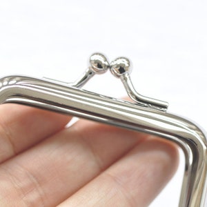 May include: Silver-toned metal purse frame with a square shape and two round knobs on the top.
