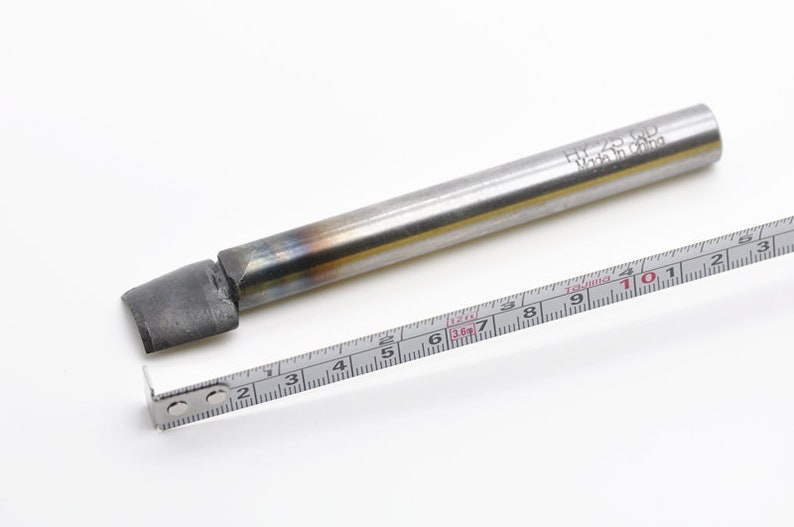 May include: A silver metal rod with a black tip, measuring approximately 10 inches long. The rod has the text "H7-25-00 Made in China" engraved on it. A measuring tape is placed next to the rod.