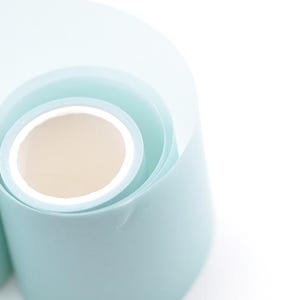 Könnte beinhalten: Nahaufnahme von zwei Rollen hellblauem Papier mit weißem Innenraum. Das Papier ist gerollt und gibt den inneren Kern frei. Der Hintergrund ist weiß und sorgt für eine saubere und minimalistische Ästhetik. Das Papier hat eine glatte Textur.