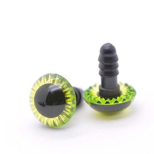 May include: Two green and yellow plastic safety eyes with black pupils and a black plastic back for attaching to a stuffed animal or craft project.