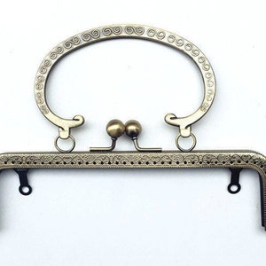 Puede incluir: Un marco de bolso de metal dorado con un asa superior decorativa y un diseño detallado y adornado. El marco está diseñado para ser utilizado para crear un bolso o bolso personalizado.