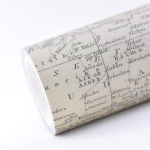 May include: A roll of adhesive tape featuring a vintage-style map print in shades of beige and black. The surface displays geographical text including names like Asben, Bilma, and Agadez, with thin black lines representing borders and grid coordinates.