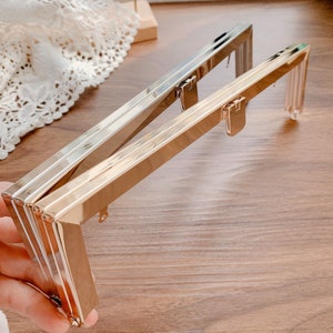 May include: Two gold-toned metal purse frames with a clasp closure. The frames are stacked on top of each other.