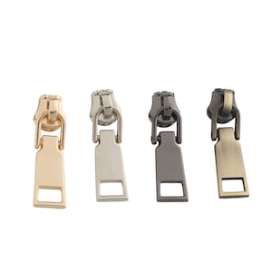 May include: Four zipper pulls in different finishes: gold, silver, black, and antique brass. Each pull has a rectangular shape with a small opening at the top.