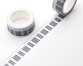 May include: Two rolls of decorative washi tape with a piano keyboard design. One roll is unraveled, displaying the black and white keys. The other roll is intact, showing the keyboard pattern around the roll. The tape is on a white background.