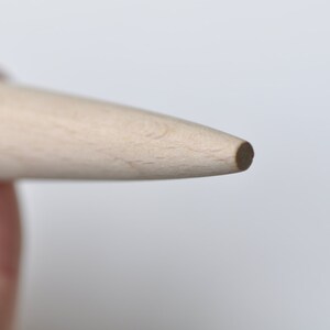 May include: Close-up of the tip of a wooden rolling pin. The tip is rounded and smooth.