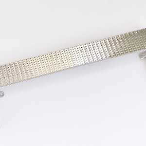 May include: A silver metal frame with a patterned design. The frame is made of a thin metal and has a rectangular shape. The frame is designed to hold a picture or other artwork.