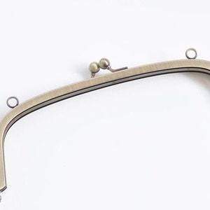 May include: A gold-toned metal purse frame with two loops on each side and a decorative knob on the top.