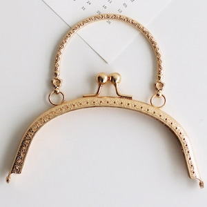 May include: Gold-toned metal purse frame with a decorative design and a top handle. The frame is designed to be used for crafting purses and bags.
