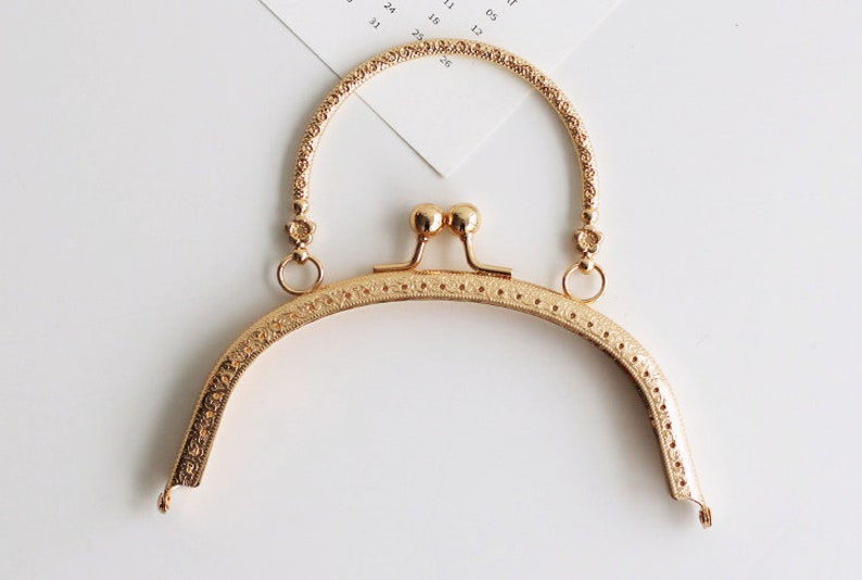 May include: Gold-toned metal purse frame with a decorative design and a top handle. The frame is designed to be used for crafting purses and bags.