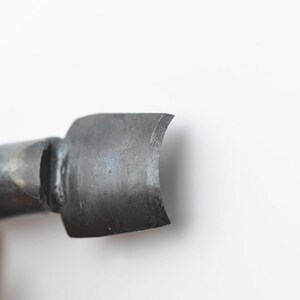 May include: Close-up of a metal tool with a curved, flat blade. The blade is dull and has a slight patina.