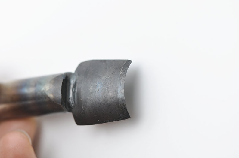 May include: Close-up of a metal tool with a curved, flat blade. The blade is dull and has a slight patina.