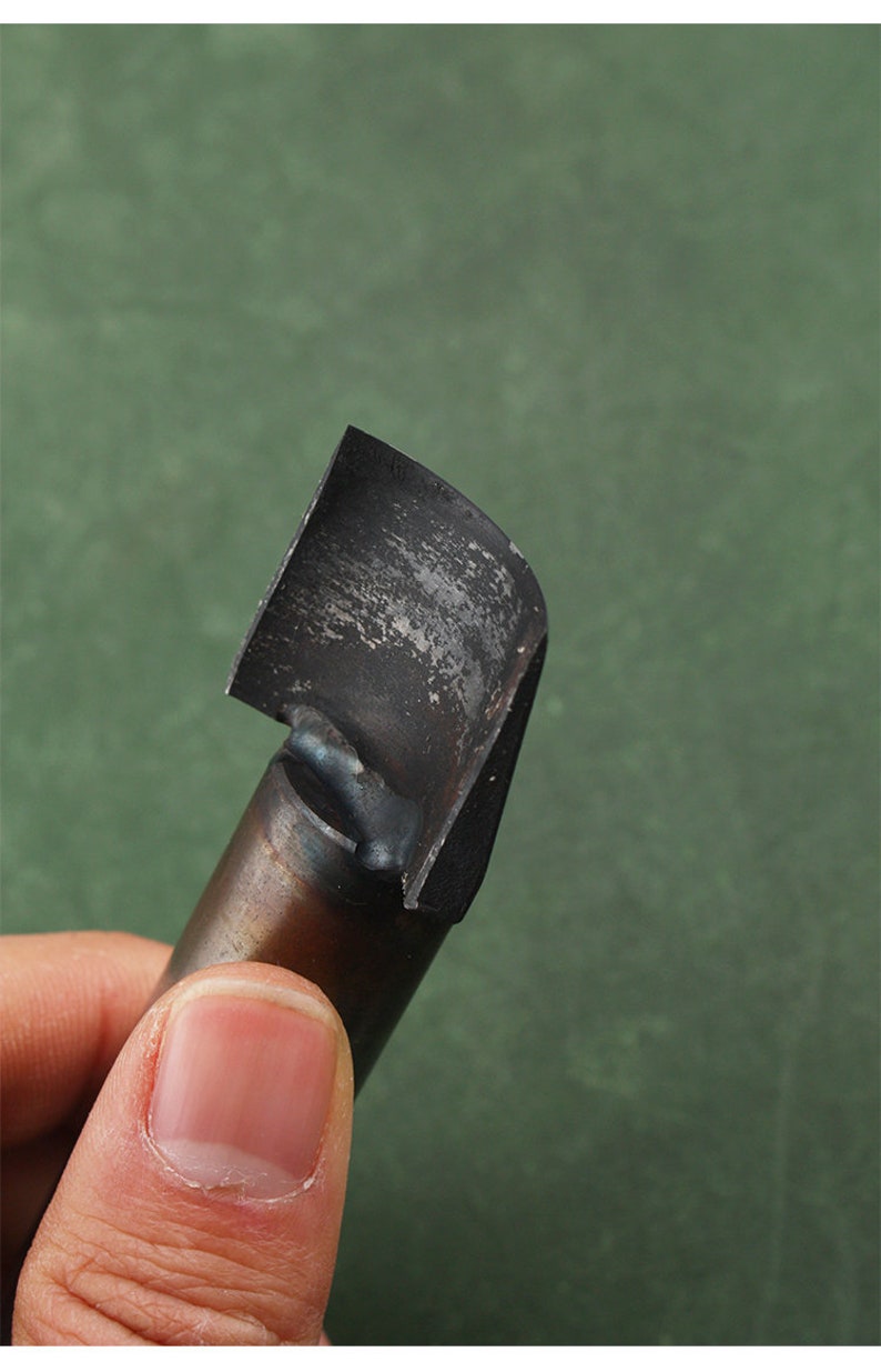 May include: A close-up of a black metal woodworking tool with a curved blade. The tool is held in a hand.