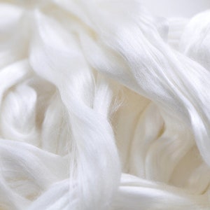 May include: Close-up of a pile of soft, white silk fibers. The fibers are tightly packed and have a smooth, flowing texture. The image highlights the natural sheen and delicate appearance of the silk, suggesting its use in textiles or crafting.