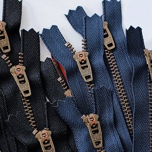 K&ouml;nnte beinhalten: Nahaufnahme einer Gruppe von schwarzen und blauen Rei&szlig;verschl&uuml;ssen mit Messing-Zierb&auml;ndern. Die Rei&szlig;verschl&uuml;sse sind in einem zuf&auml;lligen Muster angeordnet und alle ge&ouml;ffnet.