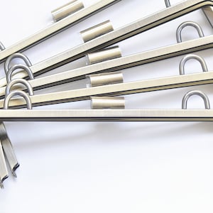 Puede incluir: Seis marcos de bolso de metal plateado con la parte superior redondeada y un gancho a cada lado. Los marcos están apilados uno encima del otro.