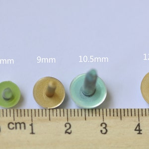 May include: Four metal buttons in different sizes, 7.5mm, 9mm, 10.5mm, and 12mm, with a ruler for scale. The buttons are gold, green, and blue.