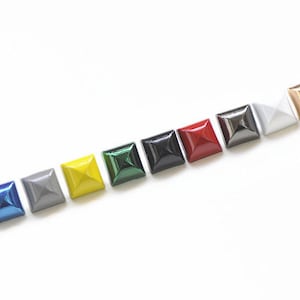 Op de afbeelding: Tien piramidevormige studs in verschillende kleuren, waaronder zilver, goud, zwart, rood, groen, blauw, geel en grijs.