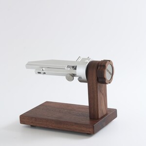 May include: A silver fly tying vise with a wooden base. The vise has a knob with the text "The Vise" on it.