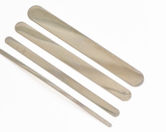 May include: Four silver metal spatulas of varying lengths, arranged in a fan shape on a white background.