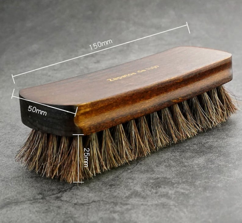 K&ouml;nnte beinhalten: Eine braune Schuhb&uuml;rste aus Holz mit einer B&uuml;rste aus Naturborsten. Die B&uuml;rste ist 150 mm lang, 50 mm breit und 25 mm dick. Die B&uuml;rste tr&auml;gt den Aufdruck "Zapateros de lujo" auf dem Holz.