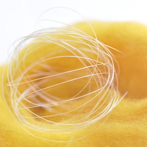 以下が含まれることがあります： 明るい黄色のテクスチャード加工された素材の上に巻かれた、透明で細い糸または紐のボールのクローズアップ。背景は柔らかくぼやけた白です。