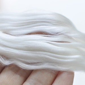 May include: Close-up of a handful of soft, white fiber. The fibers are long, flowing, and have a silky texture. The color is a bright, clean white, suggesting a natural material. The image is well-lit, highlighting the texture and quality of the fiber.