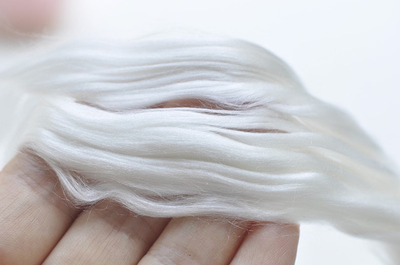 May include: Close-up of a handful of soft, white fiber. The fibers are long, flowing, and have a silky texture. The color is a bright, clean white, suggesting a natural material. The image is well-lit, highlighting the texture and quality of the fiber.