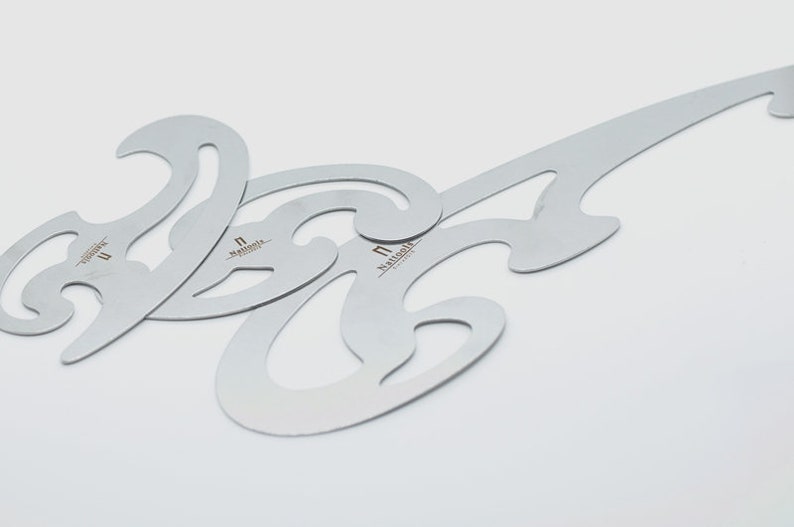 May include: Three silver metal stencils for creating decorative patterns. The stencils are shaped like a series of curves and loops. The word "remarkable" is printed on each stencil.