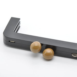 May include: Black U-shaped bag handle with two brown plastic knobs. The handle is made of a smooth, hard plastic.