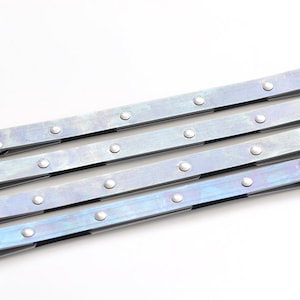 May include: Four silver metal straps with rivets and a hinge at one end. The straps are arranged in a stack, with the top strap slightly offset from the others.