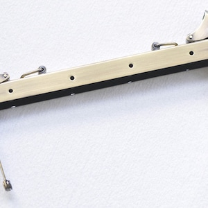 Könnte beinhalten: Ein goldfarbener Metall-Handtaschenrahmen mit zwei Scharnieren und zwei ausziehbaren Metallarmen. Der Rahmen ist so konzipiert, dass er an einer Handtasche oder einer Handtasche befestigt werden kann.