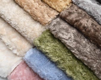 May include: A collection of colorful faux fur fabric swatches in various shades. The swatches include cream, tan, brown, gray, green, blue, and pink. The fabric has a soft, textured appearance, with visible fibers and a plush feel. Ideal for craft projects.