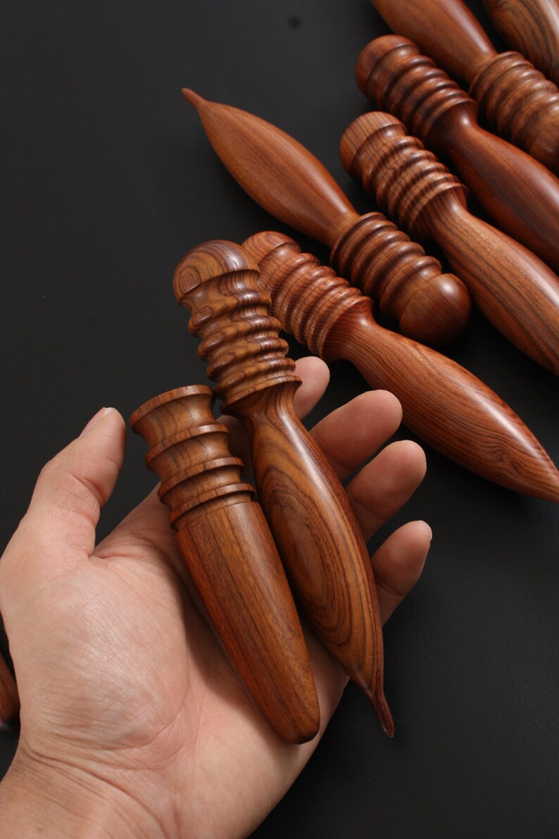 May include: A set of five wooden massage tools with different shapes and textures. The tools are made of dark brown wood with a reddish hue and have a smooth, polished finish.