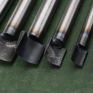 May include: Four metal leather punches of different sizes, with the largest punch on the left and the smallest on the right. The punches are on a green surface.