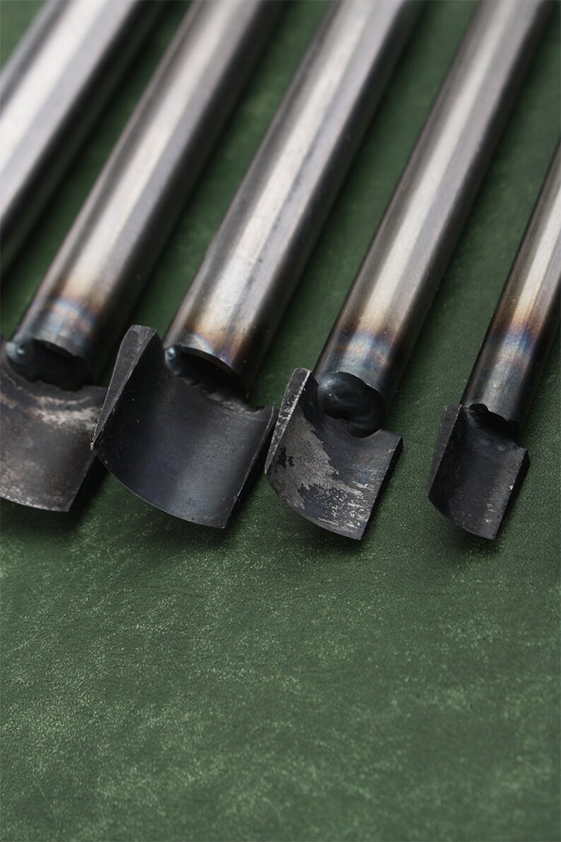 May include: Four metal leather punches of different sizes, with the largest punch on the left and the smallest on the right. The punches are on a green surface.