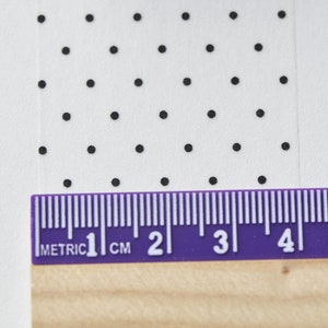 May include: A close-up of a white surface with a repeating pattern of black dots. A purple ruler with metric measurements is placed at the bottom, showing 1 cm to 5 cm.