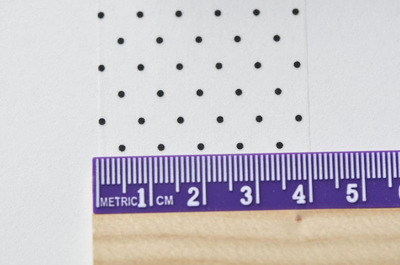 May include: A close-up of a white surface with a repeating pattern of black dots. A purple ruler with metric measurements is placed at the bottom, showing 1 cm to 5 cm.