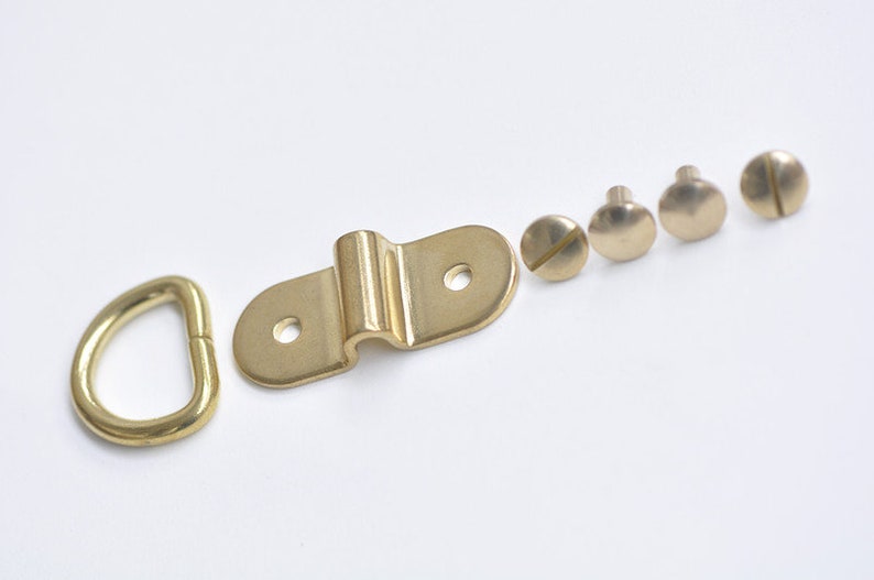 May include: A set of brass hardware for hanging items, including a D-ring, a hook, and four screws.