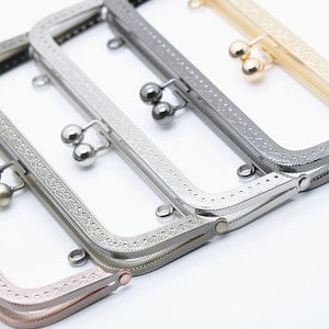 May include: Four different coloured metal purse frames with decorative edges and a clasp closure. The frames are arranged in a row, with the gold frame at the top and the rose gold frame at the bottom.