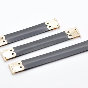 Puede incluir: Tres hebillas de correa de metal negro y dorado. Las hebillas están diseñadas para ser usadas en bolsos o carteras.