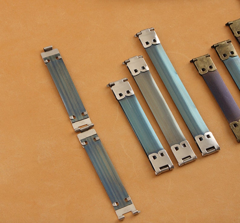 May include: Five metal strap buckles in various shades of blue and purple. The buckles are made of metal and have a brushed finish. The buckles are all the same size and shape, but they have different colors.