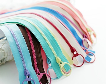 May include: Assortment of colourful zipper pulls with metal rings. The zippers are in various colours, including blue, green, pink, brown, and white.